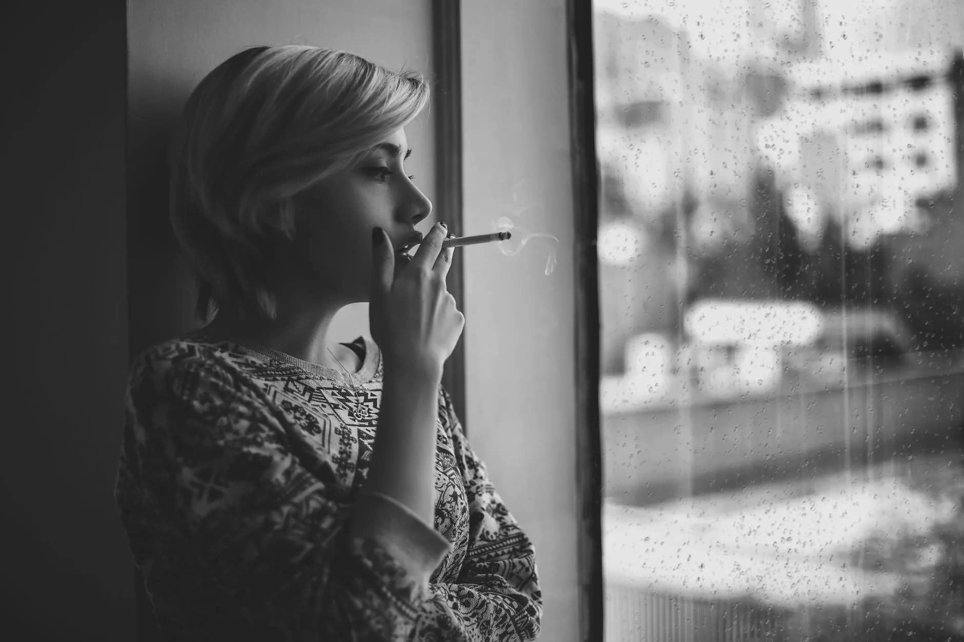 Black and white depressed female with short haircut smoking cigarette and looking out window at rainy city · Фото: Amir SeilSepour / Pexels